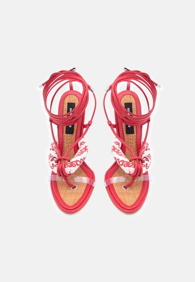 Paire de sandales rouges à brides avec semelles tissées, brides rembourrées à motif blanc, bandes claires pour les orteils et longs lacets à nouer autour de la cheville.