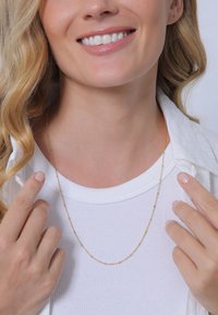 Collier en chaîne dorée avec de petites perles régulièrement espacées, porté sur une chemise blanche à côtes, avec une finition naturelle et une texture fine.