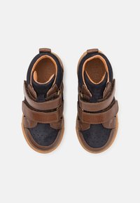 Brązowe i czarne buciki dla niemowląt z podwójnymi paskami na rzepy i gumowymi podeszwami, widok z góry na białym tle.