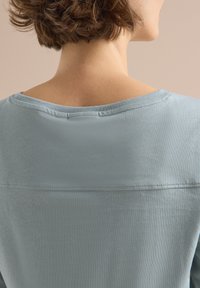 Light blue short-sleeve top with a wide neckline, featuring a smooth texture and a horizontal seam across the back.
