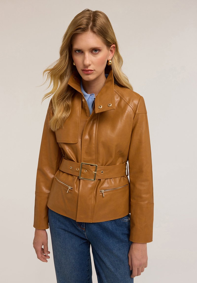Veste en cuir brun avec une taille ceinturée, un col montant et des poches zippées. Texture lisse et design ajusté.