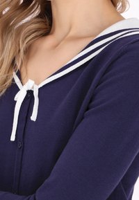 Námořnický svetr s bílým pruhovaným límečkem, zapínáním na knoflíky a předním zavázáním. Měkká textura s dlouhými rukávy.