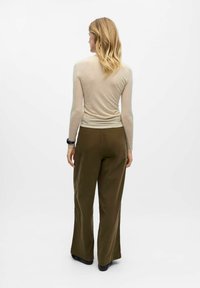 Langærmet beige top sat sammen med olivengrønne vide bukser, der har en glat tekstur og en afslappet pasform. Sorte sko fuldender outfittet.