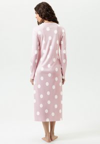 Nachthemd mit langen Ärmeln aus hellrosa Stoff mit großen weißen Punkten. Knöchellang, mit glatter Textur und lockerem Schnitt.
