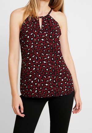 Femme portant un haut sans manches bordeaux avec imprimé léopard noir et blanc et encolure en forme de goutte, associée à un pantalon noir.