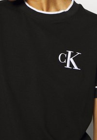 Svart bomulls t-shirt med rund hals, vit kant och broderad "cK" logotyp på vänster bröst. Mjuk textur och avslappnad passform.