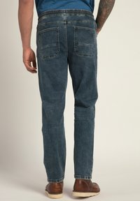 Jeans de mezclilla con un corte relajado, color azul medio, cinturilla elástica y dos bolsillos traseros, combinados con zapatos marrones sobre un fondo claro.