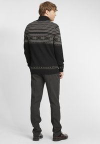 Suéter de punto negro con bandas horizontales de patrones en gris, blanco y rojo. Combinado con pantalones gris ajustados y zapatos marrones.