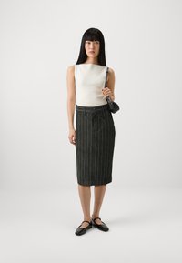 Weißes geripptes ärmelloses Oberteil, dunkelgrüner gestreifter Rock mit Taillengürtel und schwarzen Ballerinas, minimalistischem Design, einfarbiger Hintergrund.