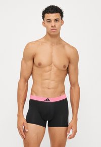 Črne bokserice s roza elastičnim pasom, na katerem je črn Adidas logotip in dodatki. Mehka, raztegljiva tkanina, zasnovana za udobje.