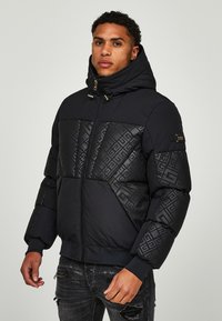 Giacca a vento nera con cappuccio, caratterizzata da un motivo geometrico trapuntato sul petto e sulle spalle. Chiusura a zip e orlo a coste.