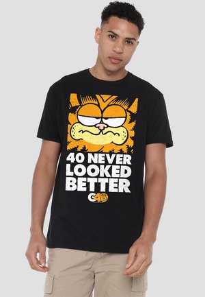 Black cotton t-shirt featuring a cartoon cat graphic with orange and white accents. Text reads "40 NEVER LOOKED BETTER" in bold white letters.