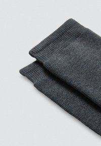 Calcetines de algodón grises con textura acanalada y puños elásticos, doblados de manera ordenada sobre un fondo gris claro.