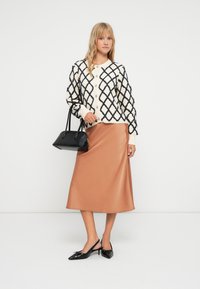 Kötött krém kardigán navy gyémánt mintával, fekete gombokkal; selymes réz szoknya; fekete slingback magassarkú cipő masni részlettel; fekete kézitáska.