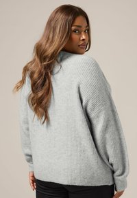 Light gray oversized sweater with a textured, ribbed knit design and dropped shoulders, paired with black pants, shown from the back.