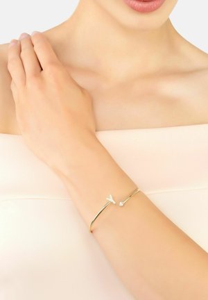 Gold open bangle bracelet featuring a delicate Y-shaped design and small crystal accent, worn on a bare arm against a soft background.
