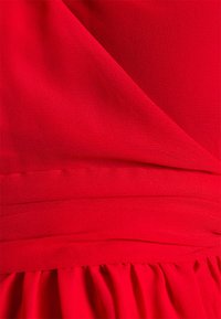 Tecido vermelho com um acabamento texturizado, apresentando elementos de design drapeado e pregas horizontais na cintura, criando um aspeto suave e fluido.