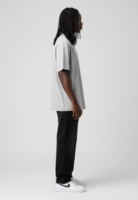 Grijze korte mouw t-shirt met een ontspannen fit, gecombineerd met zwarte straight-leg jeans en witte sneakers met een zwart Nike-logo.
