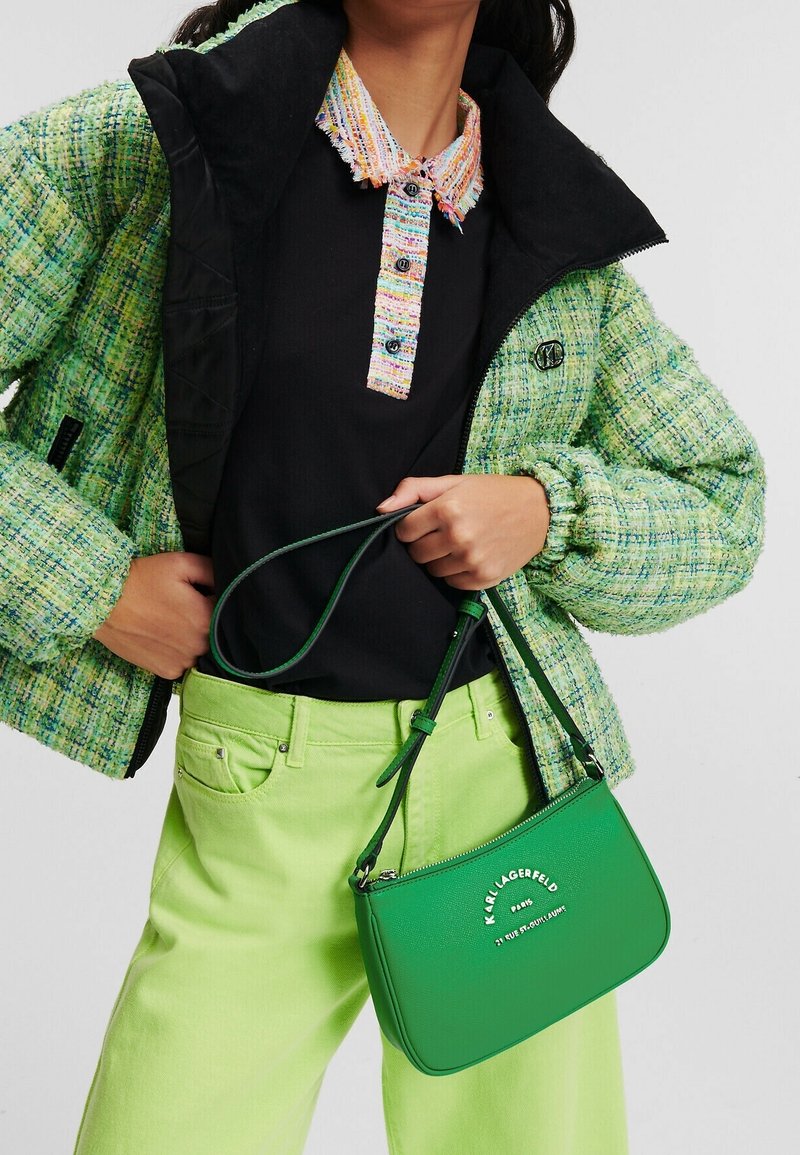Zelená kabelka s logem, doplněná o strukturovanou zeleno-černou bundu a jasně zelené kalhoty. Hlavní část obsahuje vícebarevný, třepený límec.