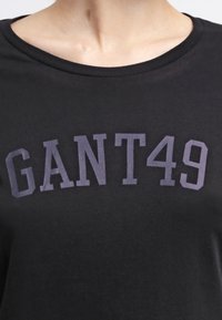 Mustat t-paita, jossa on pyöreä kaula-aukko ja suuri, kontrastoiva harmaa "GANT 49" -logo etupuolella. Pehmeä kangas, jolla on sileä pinta.