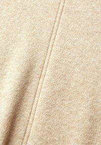 Beige gebreide stof met een zachte textuur, voorzien van een subtiel gemêleerd patroon en een zichtbare naad die verticaal langs het oppervlak loopt.