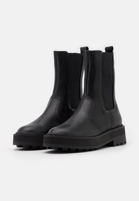 Mustat nahka-nilkkurit, joissa on elastiset sivupaneelit, massiivinen pohja ja minimalistinen muotoilu. Silkkinen pinta, jossa on vahvistettu saumaus.