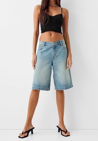 Mustapohjainen lyhyt tanktoppi, vaaleansiniset denim Bermuda-shortsit, suora leikkaus, revitty helma, yhdistetty mustiin korkokenkiin.