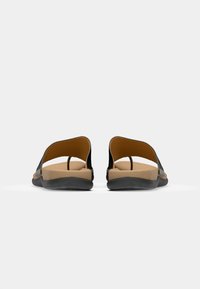 Sandales noires avec des lanières larges, semelle intérieure rembourrée marron et semelle en caoutchouc noir flexible ; design minimaliste avec un dos ouvert.