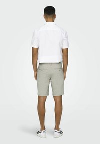 Witte overhemd met korte mouwen voor heren met een rechte snit, gecombineerd met lichtgrijze kniebange korte broek en witte sneakers. Eenvoudig ontwerp en neutrale kleuren.