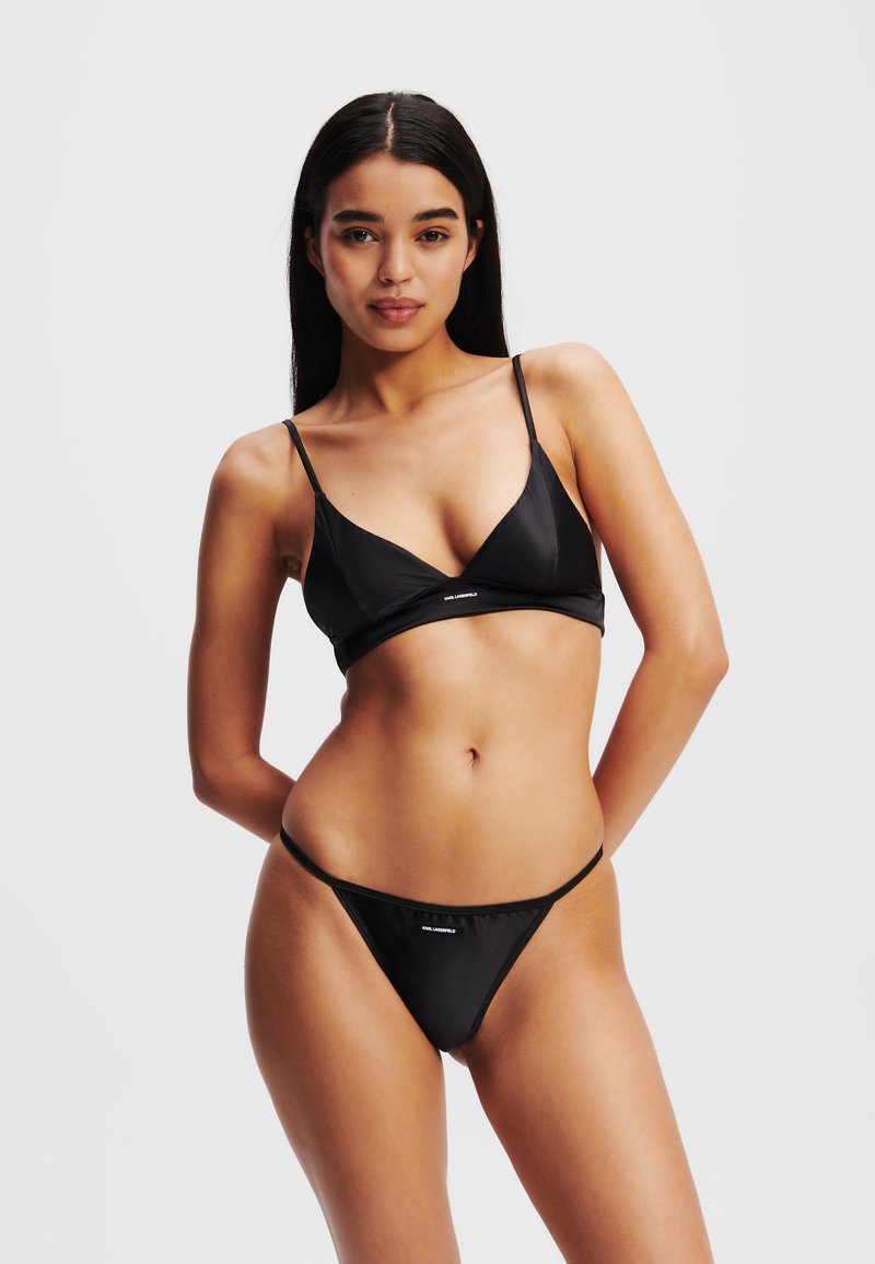 Črn bikini komplet, ki vključuje trikotni top z tankimi naramnicami in ujemajoče se tangice z minimalno pokritostjo, izdelan iz gladkega, sijočega materiala.