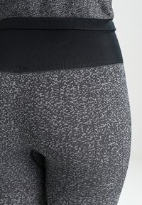 Leggings a fantasia nera e grigia con una ampia cintura nera uniforme; tessuto testurizzato con un mix di design geometrici.