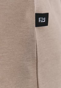 Beżowy materiał bawełniany o gładkiej fakturze; zawiera małą czarną metkę z białym napisem w górnym rogu.