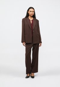 Brown tailored blazer with notched lapels and a single button, paired with matching wide-leg trousers and a dark maroon blouse. Black heels.