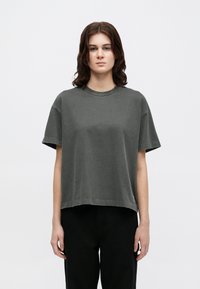 Pelēks, īsu piedurkņu kokvilnas T-krekls ar plašu kakla izgriezumu un brīvu piegriezumu. Izcila šuvju detaļa apakšmalā. Vienkāršs dizains, bez rakstiem.