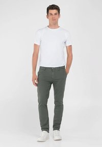 T-shirt blanche à manches courtes associée à un pantalon slim fit vert olive et des baskets blanches. Design épuré avec une palette de couleurs neutres.