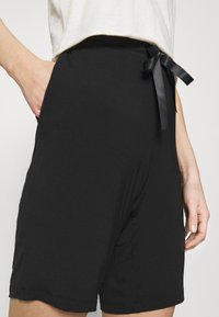 Shorts noirs en tissu doux, dotés d'une coupe ample, de poches latérales et d'un lien en satin noir à la taille pour un style ajustable.