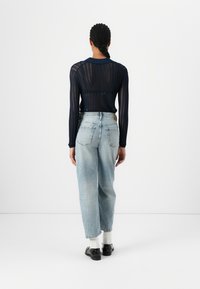 Top a maniche lunghe in rete blu navy con colletto, abbinato a jeans a vita alta blu chiaro. Scarpe nere con calzini bianchi.