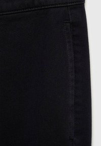 Crni denimski materijal izbliza, s suptilnim teksturiranim uzorkom i detaljima bočnog šava. Glatka površina s vidljivim šavovima.