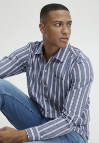 Blauw-wit gestreepte langemouwen shirt met knoopsluiting, pocketdetail en zachte textuur, gecombineerd met lichtblauwe jeans.