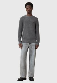 Szary sweter dzianinowy z okrągłym dekoltem, połączony z jasnoszarymi, lekko postrzępionymi spodniami o szerokich nogawkach i czarnym obuwiem.