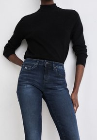 Suéter negro de manga larga con cuello alto, combinado con jeans de tiro alto en azul oscuro. El suéter es suave y los jeans presentan un ligero desgastado y un diseño clásico de cinco bolsillos.