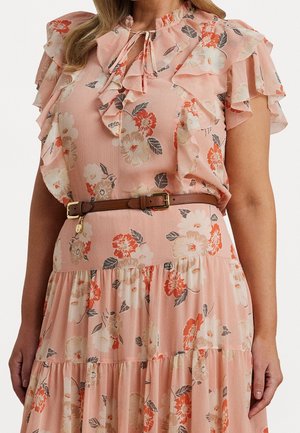Femme portant une robe fleurie rose avec des manches et un col volantés, cintrée à la taille avec une ceinture en cuir marron.