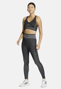 Conjunto de sujetador deportivo y leggings negros con un patrón texturizado y cintura alta. Hecho de material elástico; los acentos incluyen el logo de Adidas.