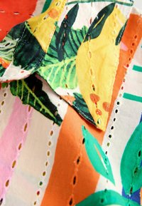 Tela colorida con un patrón floral que presenta hojas amarillas y verdes, con secciones a rayas en naranja, rosa y blanco, y costuras decorativas.