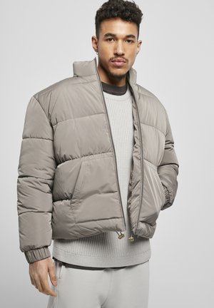 Chaqueta acolchada hecha de un material suave y gris claro, con un alto cuello, puños elásticos y un cierre de cremallera con bolsillos laterales.