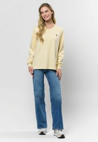 Griesta ar V veida kaklu, garām piedurknēm, izgatavota no mīksta materiāla; ar izšūtu dizainu kreisajā krūtīs. Apvienota ar zilām džinsam.