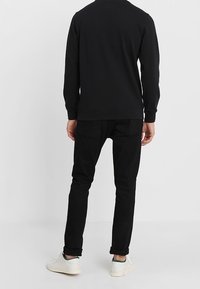 Svart pullovertröja med rund halsringning, tillsammans med svarta slim-fit jeans. Vita sneakers med gröna accenter. Enkel design, inga synliga logotyper.