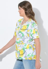 Top corto bianco a maniche corte con contorni neri di tartarughe e limoni in verde e giallo. Design a V con vestibilità rilassata e spacchi laterali.