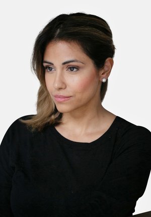 Schwarzes Langarmshirt, glattes Material. Lange, glatte Haare mit sanften Wellen. Runde Perlenohrringe. Neutraler Hintergrund. Fokus auf das Gesicht und den Ausdruck.