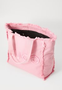 Roze canvas draagtas met rafelige randen, geborduurd logodetail en dubbele stoffen handvatten. De binnenkant is gevoerd met een zwarte voering.